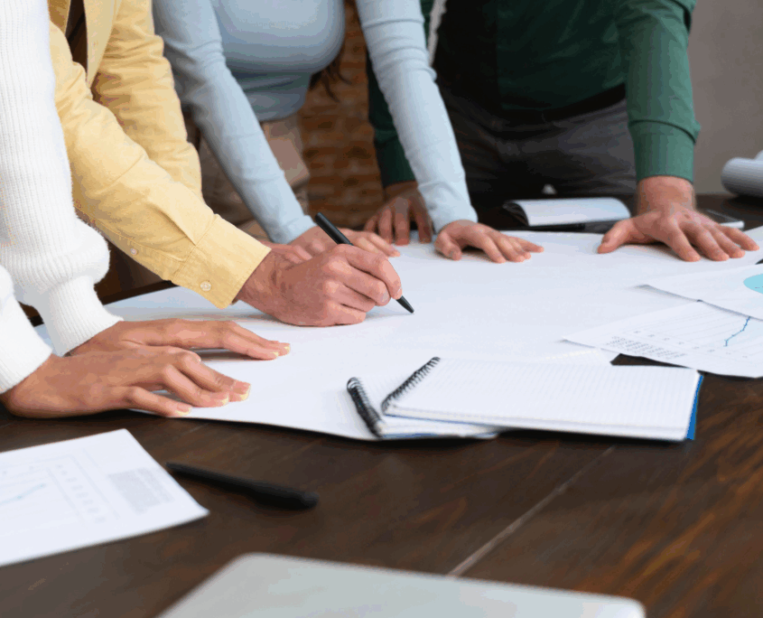 Focus sulle mani di persone, appoggiate a un tavolo, che consultano tutta una serie di documenti