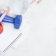 Immagine che raffigura una mela, un peso per attività fisica, bicchiere di acqua e blocco di carta con penna